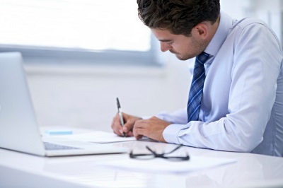 Angestellter arbeitet am Schreibtisch mit Laptop und Stift