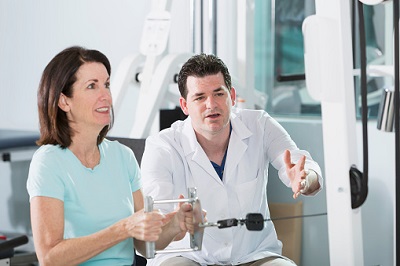 Ältere Patientin macht Kraftübung zusammen mit Physiotherapeut.